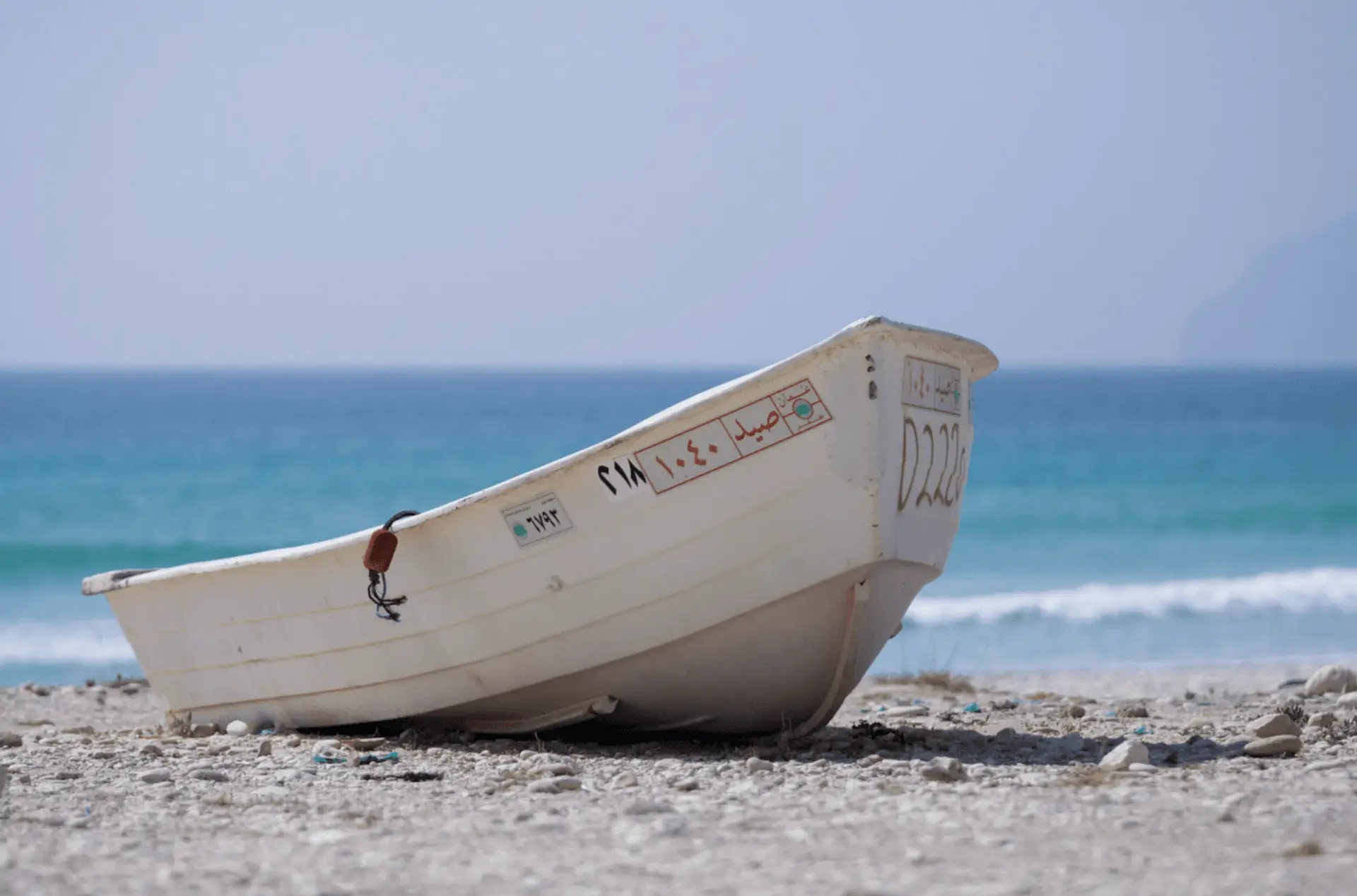 Barque de pêcheur blanche sur le sable d'une plage sauvage du Dhofar bordée par l'océan Indien à Salalah, Oman.