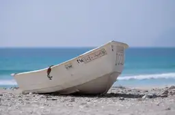 Barque de pêcheur blanche sur le sable d'une plage sauvage du Dhofar bordée par l'océan Indien à Salalah, Oman.