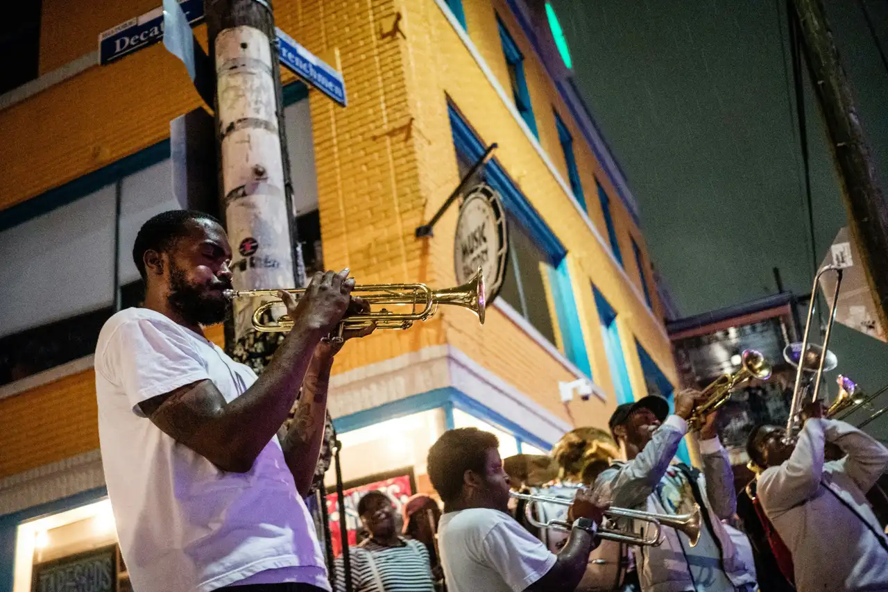 Musicien jouant de la trompette de nuit dans une rue animée de La Nouvelle-Orléans avec d'autres cuivres en arrière-plan