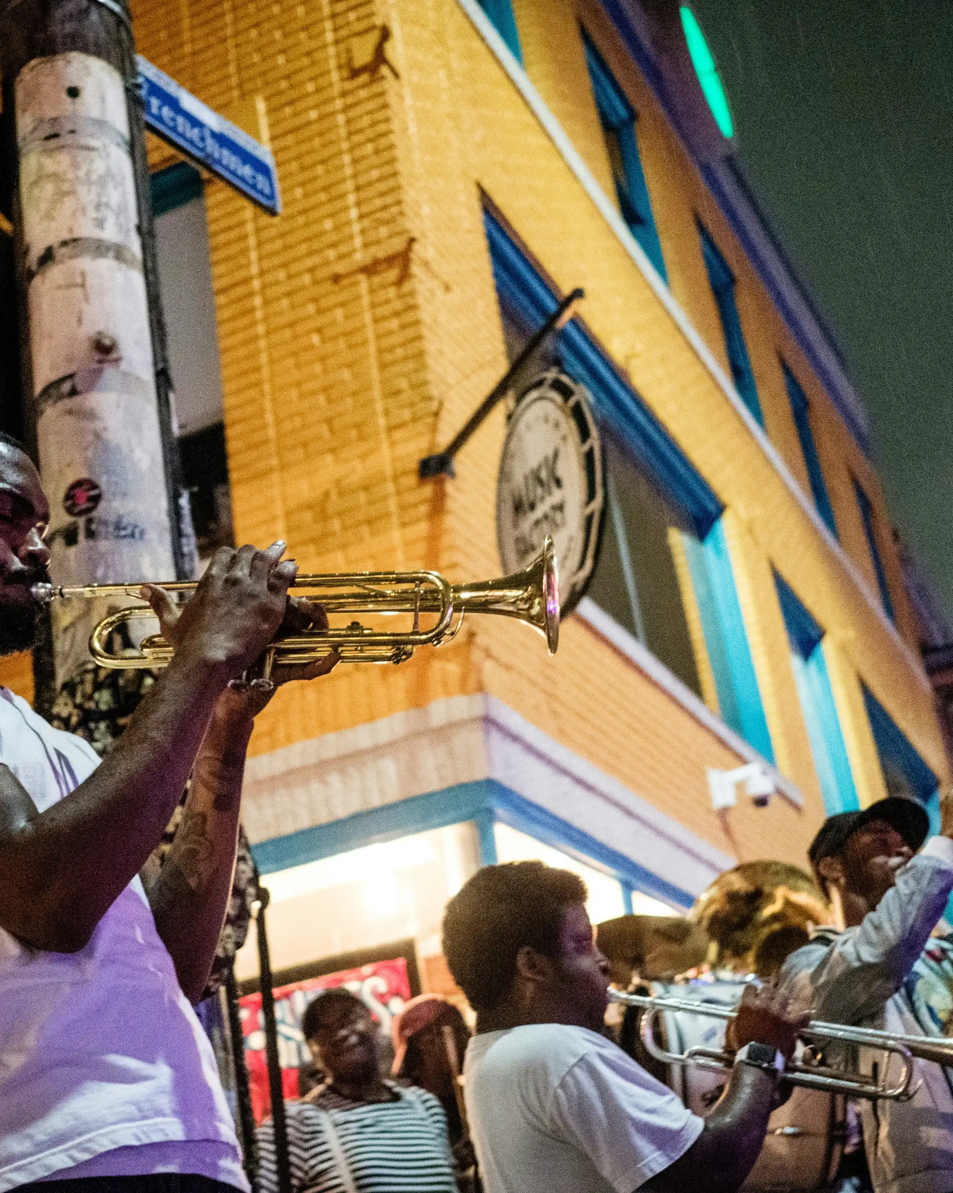 Musicien jouant de la trompette de nuit dans une rue animée de La Nouvelle-Orléans avec d'autres cuivres en arrière-plan