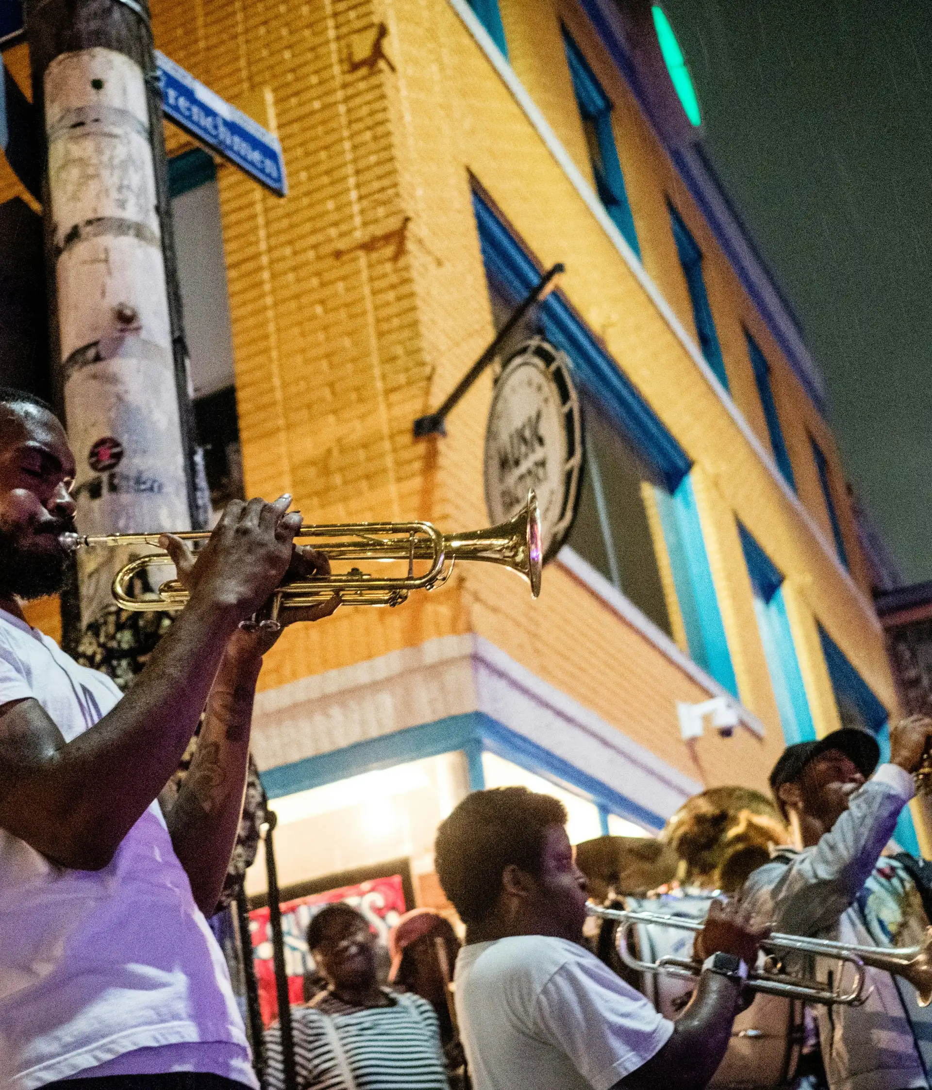 Musicien jouant de la trompette de nuit dans une rue animée de La Nouvelle-Orléans avec d'autres cuivres en arrière-plan