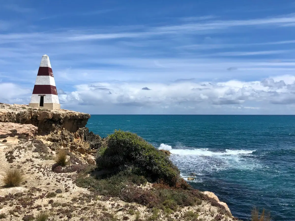 Balise de navigation pyramidale rayée rouge et blanche sur une falaise surplombant l'océan à Robe