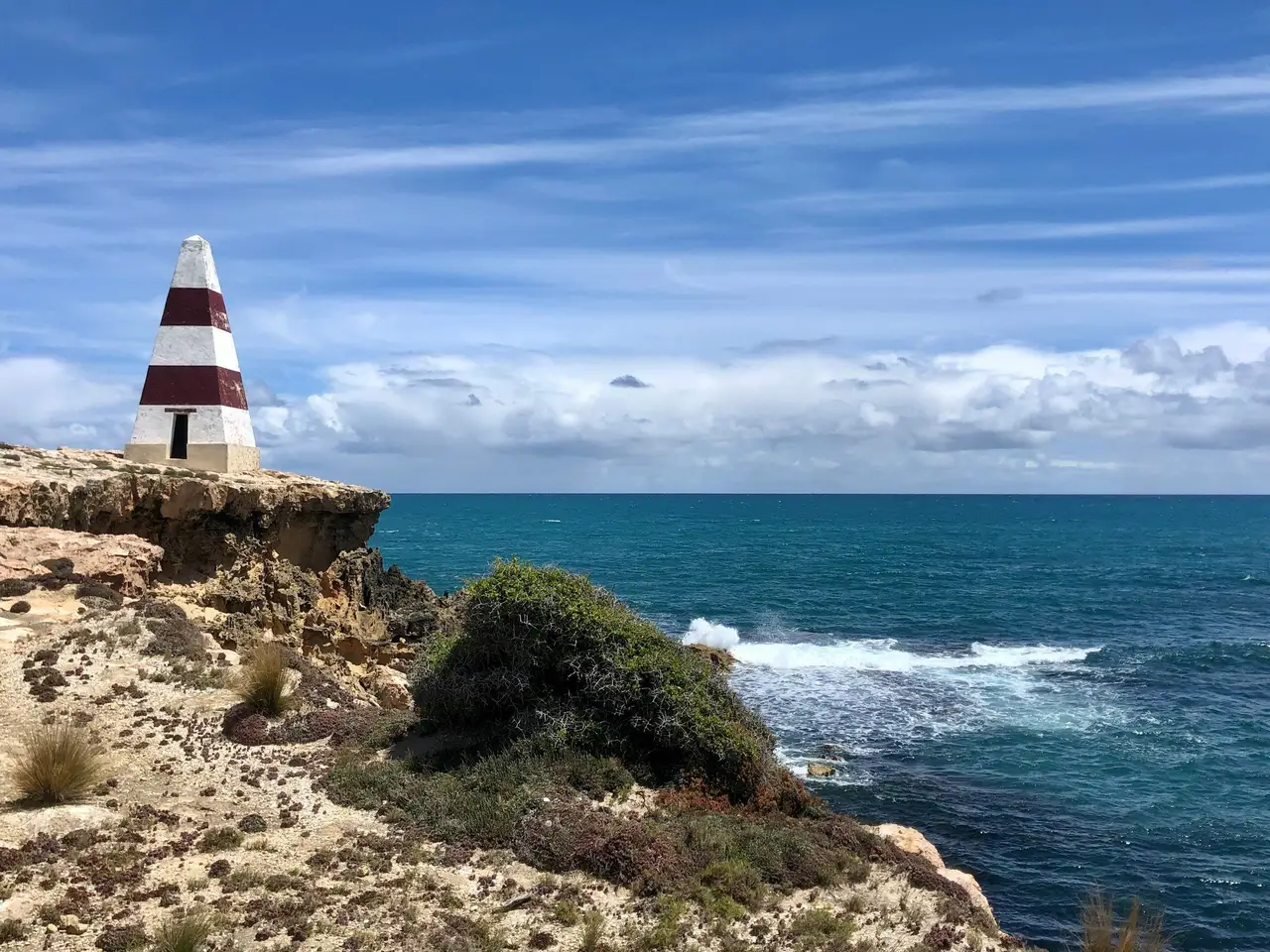 Balise de navigation pyramidale rayée rouge et blanche sur une falaise surplombant l'océan à Robe