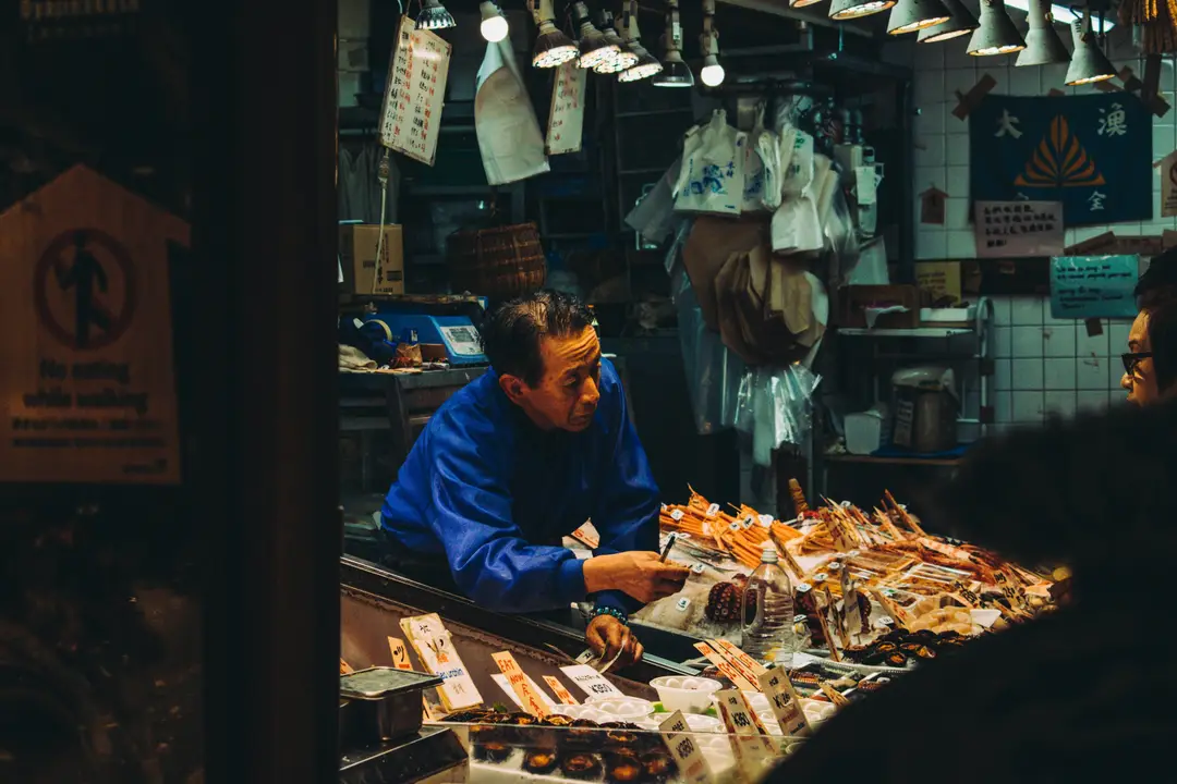 Commerçant préparant des brochettes de produits frais sur son étal au marché couvert de Nishiki à Kyoto.