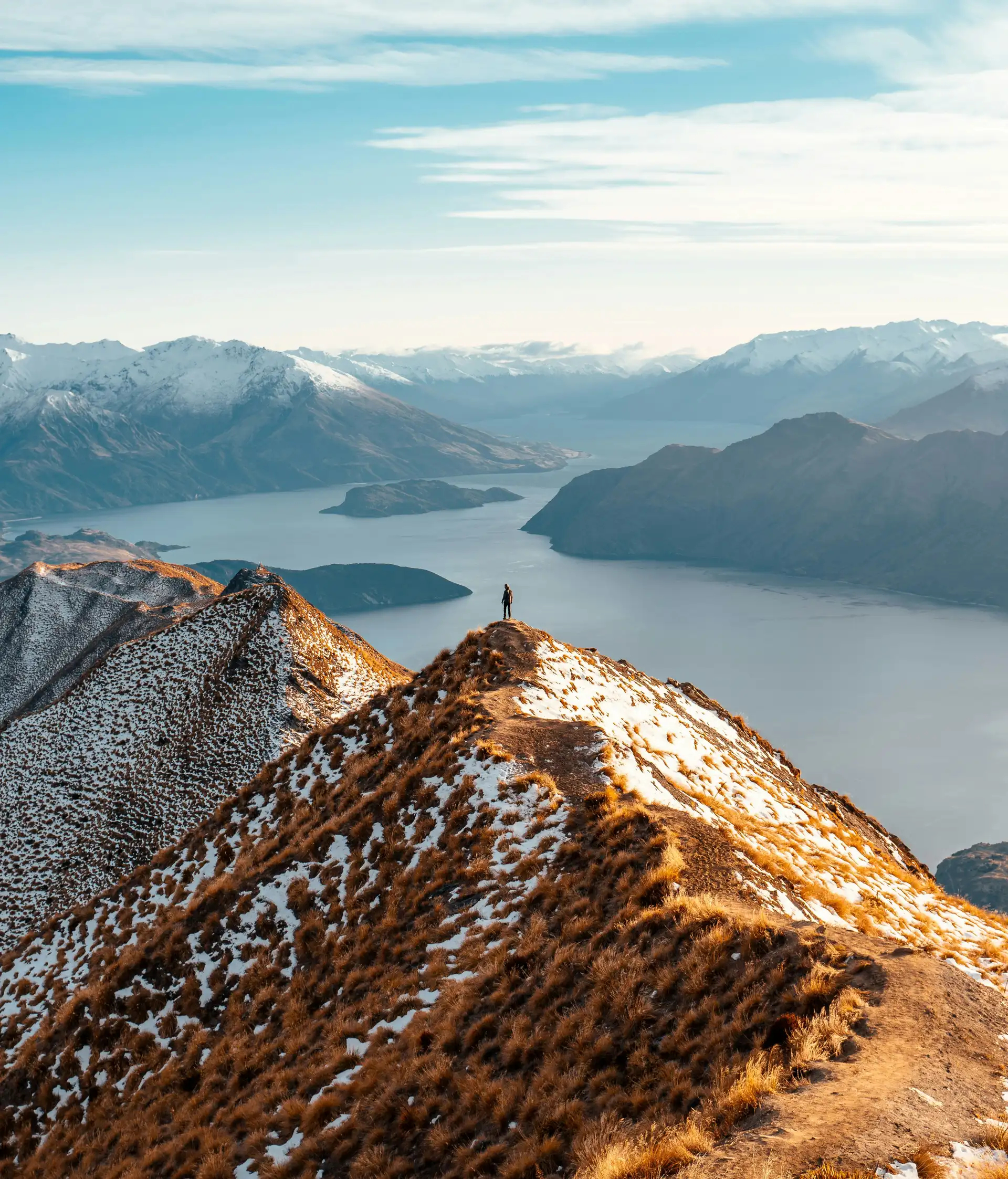 Randonneur contemplant la vue panoramique sur le lac Wanaka et les montagnes depuis le sommet de Roys Peak.