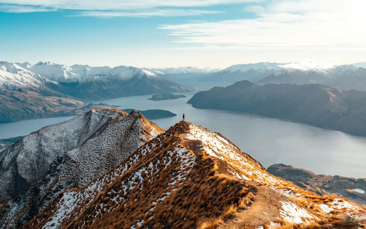 Randonneur contemplant la vue panoramique sur le lac Wanaka et les montagnes depuis le sommet de Roys Peak.