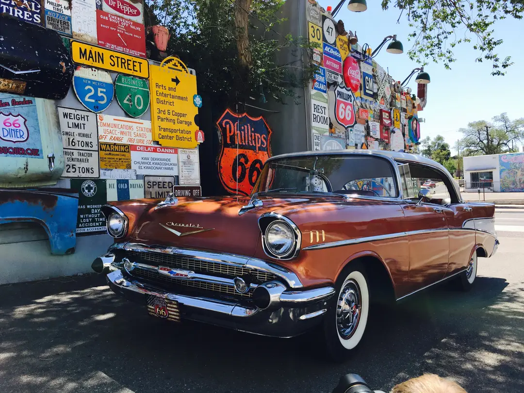 Une Chevrolet ancienne devant des panneaux de la Route 66.
