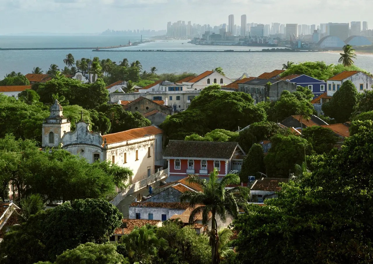 Voyage au Brésil – Vue aérienne panoramique sur les toits historiques d'Olinda et la skyline moderne de Recife bordant l'océan Atlantique au loin.