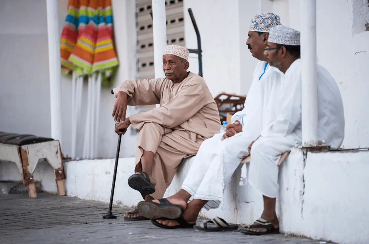 Voyage à Oman Trois hommes omanais en habit traditionnel (dishdasha) discutant dans les rues de Mascate.