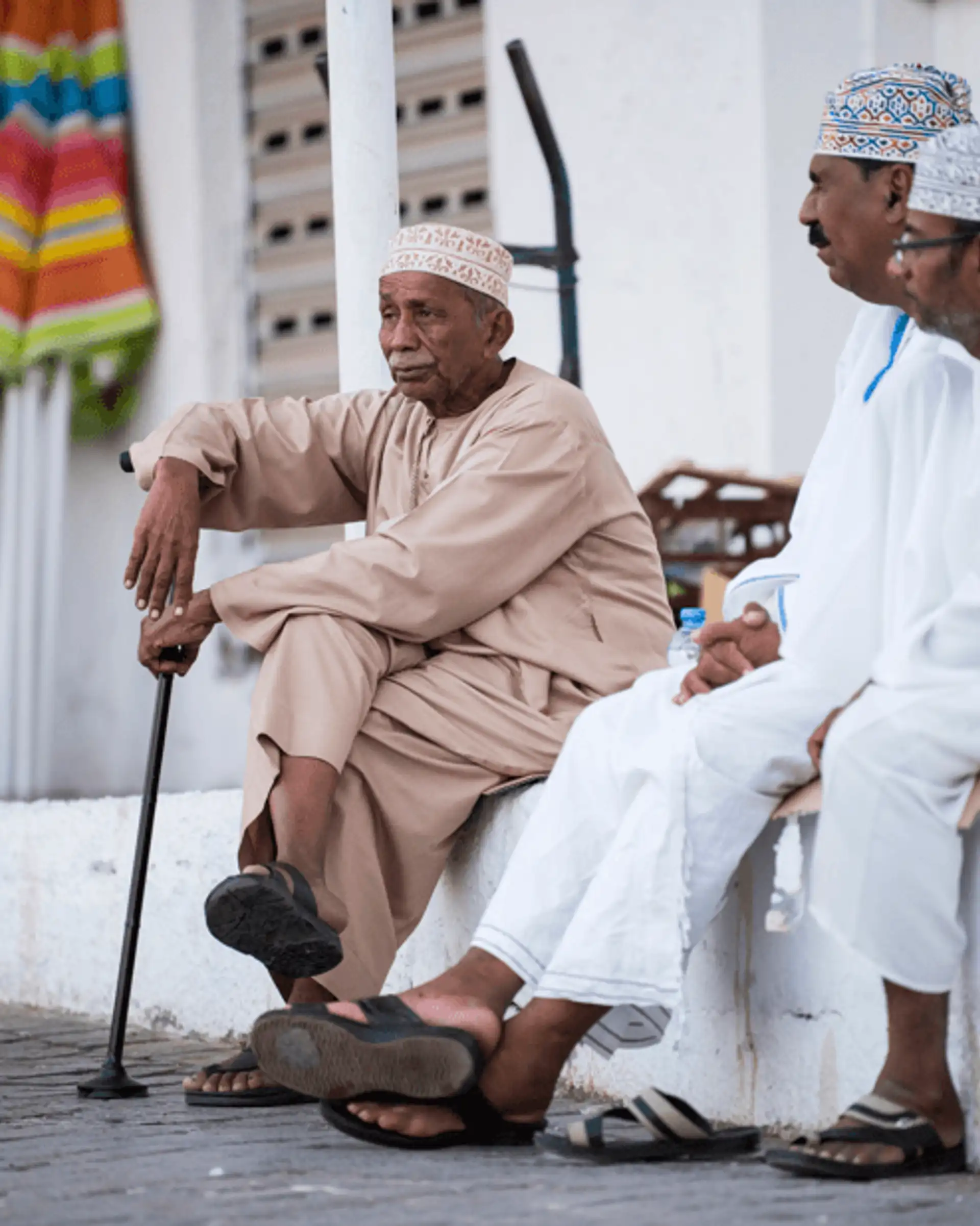 Voyage à Oman Trois hommes omanais en habit traditionnel (dishdasha) discutant dans les rues de Mascate.