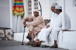 Voyage à Oman Trois hommes omanais en habit traditionnel (dishdasha) discutant dans les rues de Mascate.
