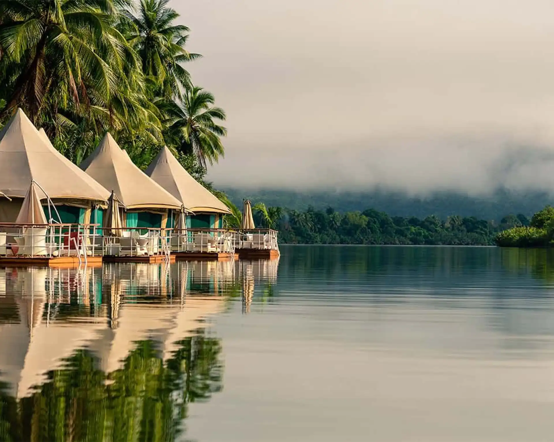 Une rangée de tentes de luxe flottantes en toile installées sur des pontons en bois au bord d'une rivière calme entourée de jungle et de brume à Koh Kong au Cambodge.