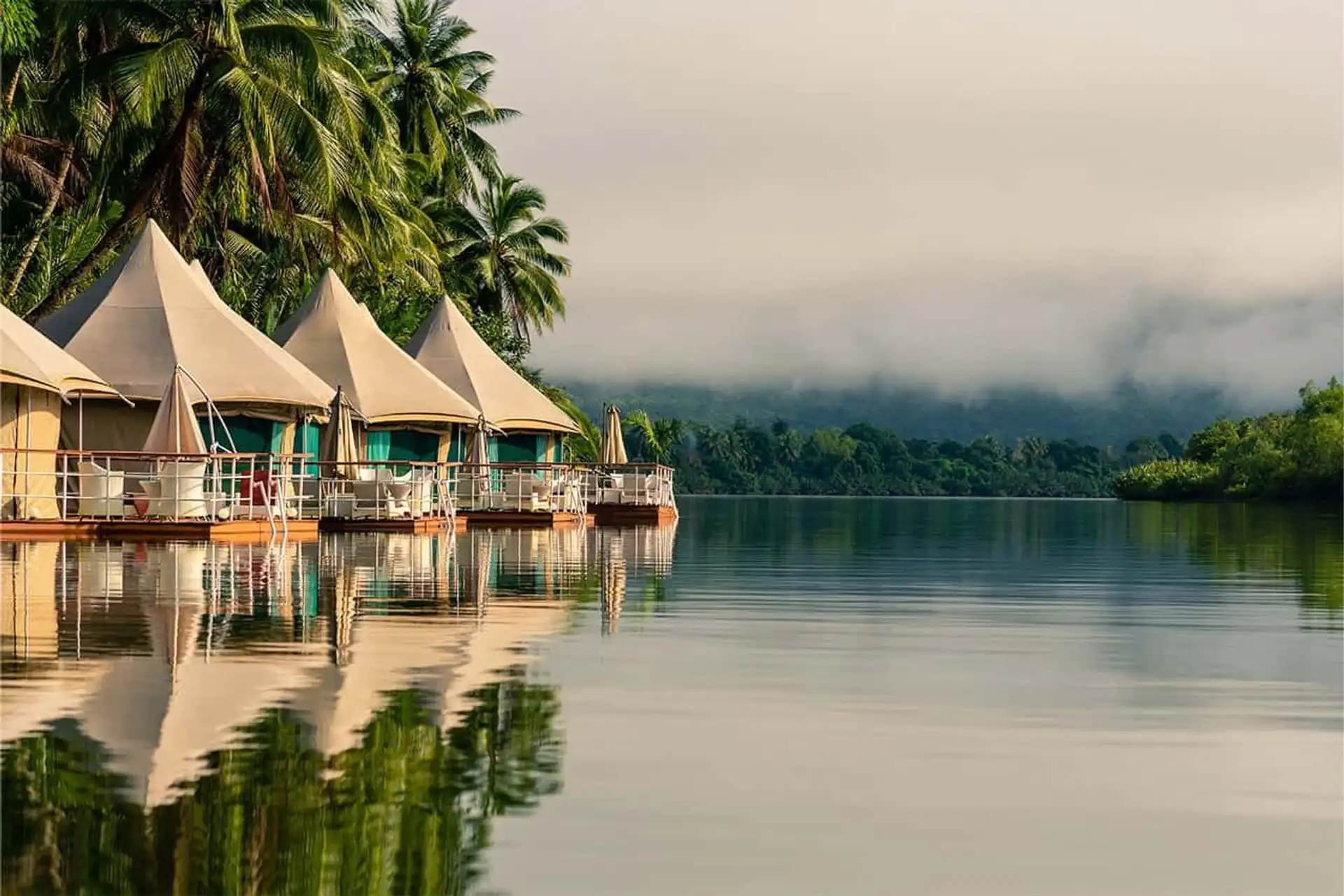 Une rangée de tentes de luxe flottantes en toile installées sur des pontons en bois au bord d'une rivière calme entourée de jungle et de brume à Koh Kong au Cambodge.