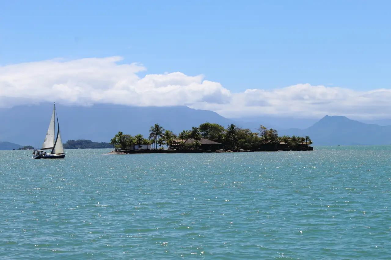 Voyage au Brésil – Un voilier blanc naviguant sur les eaux calmes de la Costa Verde près d'un îlot verdoyant dans le fjord tropical du Saco do Mamanguá à Paraty.