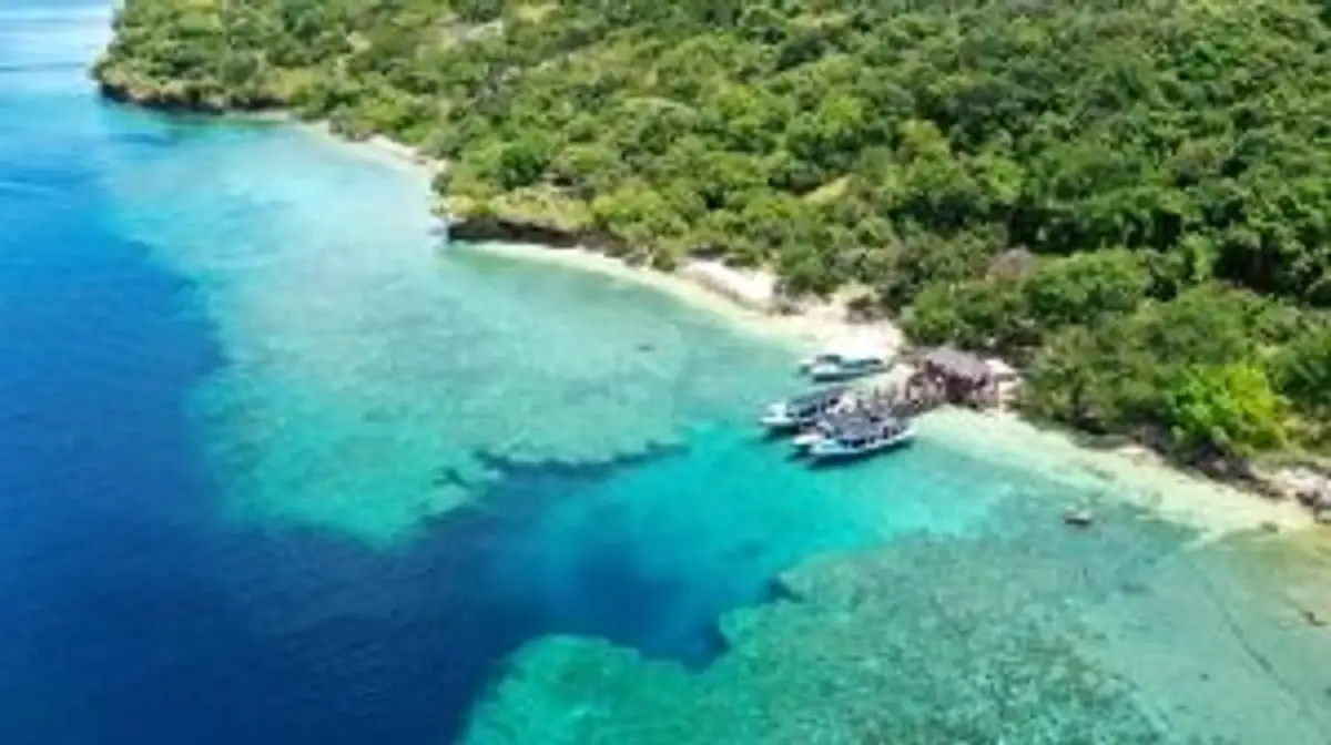 Voyage en Asie — Vue aérienne d'une baie tropicale à Bali : eaux cristallines bleu turquoise et vert émeraude, plage bordée de jungle et bateaux amarrés.
