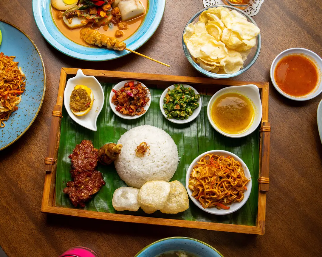 Voyage en Indonésie – Un plateau traditionnel de Nasi Campur avec du riz, des brochettes satay, des nouilles frites et du sambal pour un guide sur la gastronomie de Java et Bali.