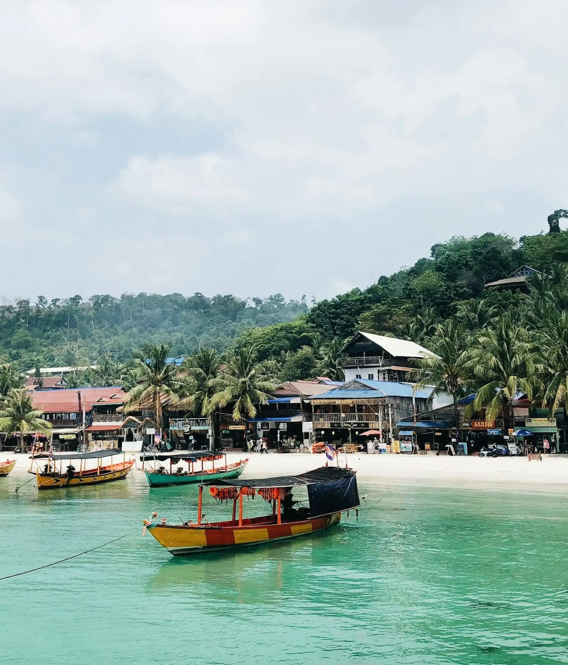 Une plage tropicale de sable fin bordée d'eaux turquoise claires et de collines verdoyantes parsemées de palmiers et de bungalows au bord de l'eau au Cambodge.