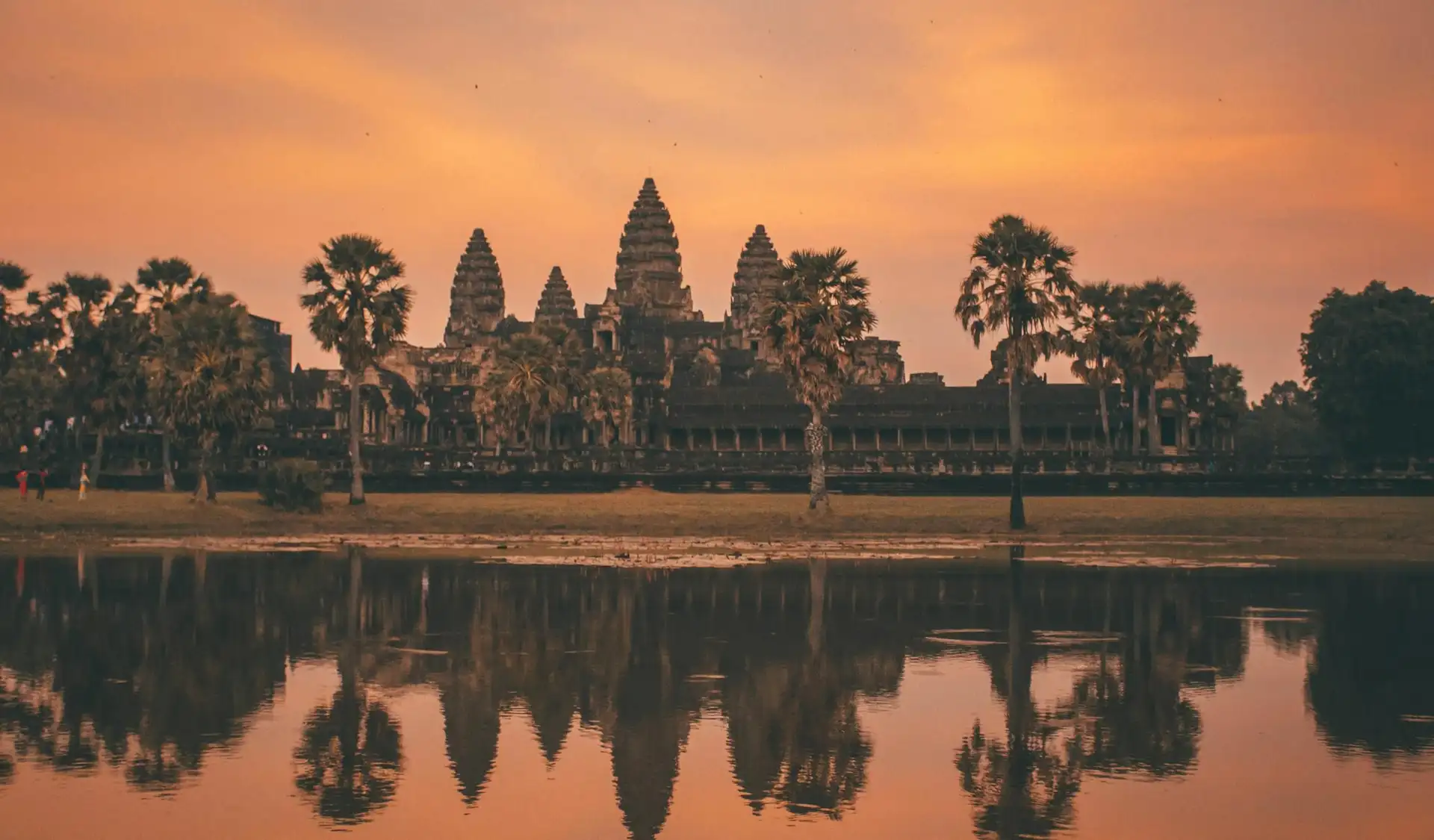 Guide voyage Cambodge – Les cinq tours emblématiques du temple d'Angkor Wat se reflétant dans l'eau sous un ciel orangé.