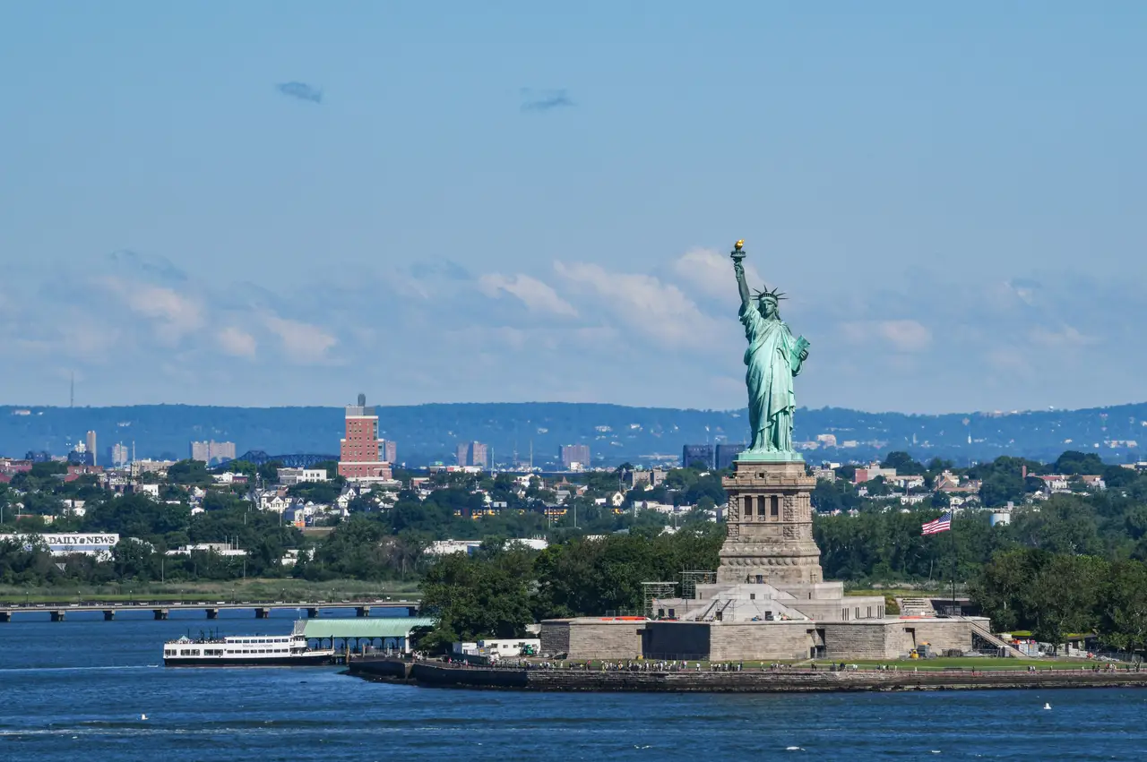 Statue de la Liberté dressée sur son socle dans le port face à l'eau bleue et la côte sous un ciel ensoleillé à New York