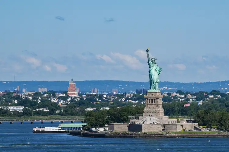 Statue de la Liberté dressée sur son socle dans le port face à l'eau bleue et la côte sous un ciel ensoleillé à New York