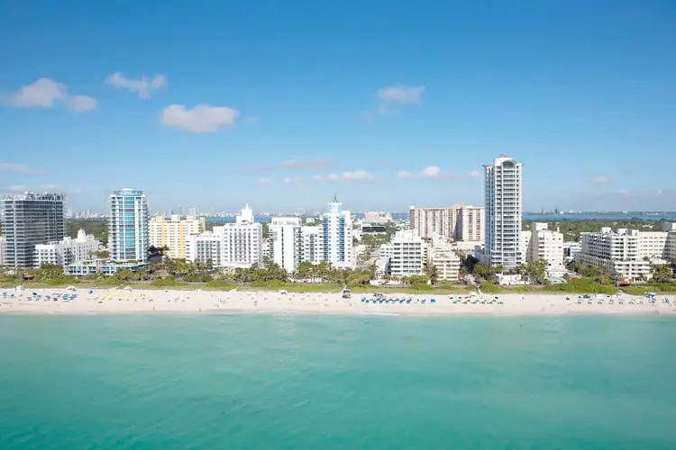 Vue panoramique sur la plage de sable blanc et la skyline d'immeubles de Miami Beach bordée par une eau turquoise sous un ciel bleu