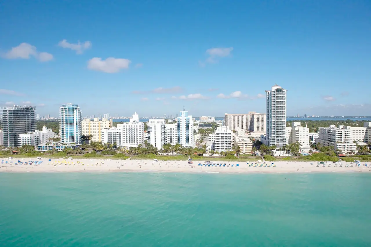 Vue panoramique sur la plage de sable blanc et la skyline d'immeubles de Miami Beach bordée par une eau turquoise sous un ciel bleu