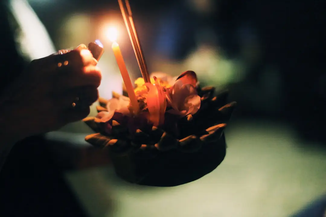 Mains allumant la bougie d'une composition artisanale de fleurs et de feuilles de bananier lors d'une fête traditionnelle au Laos.
