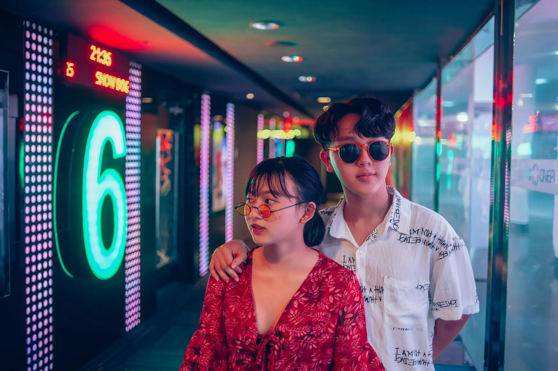 Couple devant des enseignes lumineuses et néons colorés dans une rue animée du Vietnam à la nuit tombée.