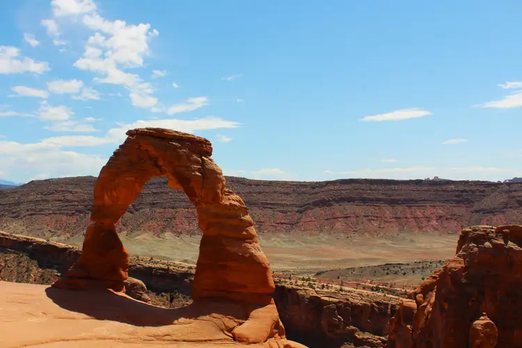 Arche naturelle en grès rouge de Delicate Arch se dressant face aux canyons désertiques sous un ciel bleu près de Moab