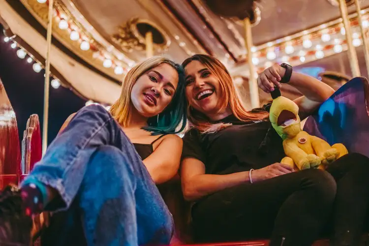 Deux amies souriantes assises sur un manège de parc d'attractions avec une peluche à Orlando