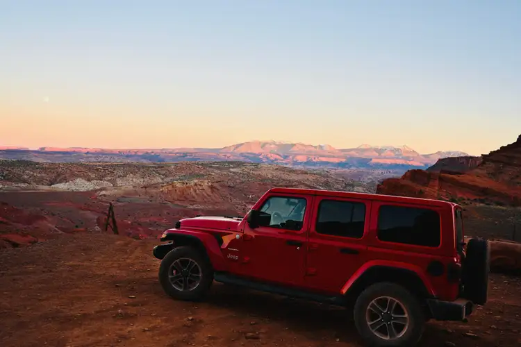 Véhicule tout-terrain rouge stationné sur une crête rocheuse face à l'immensité des canyons au coucher du soleil à Moab