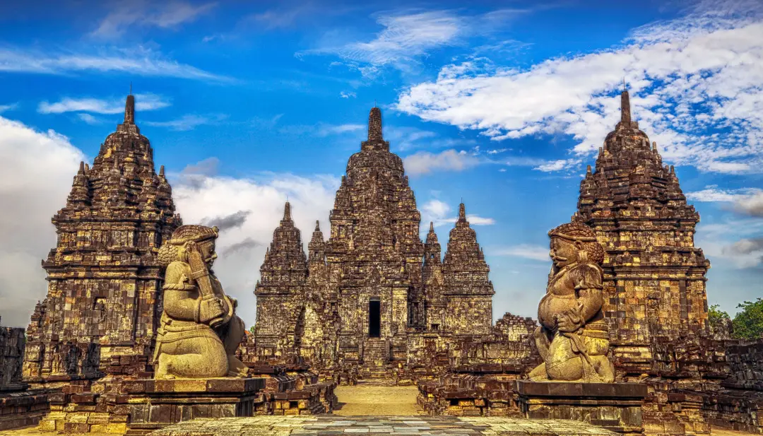 Voyage à Java – Les statues de gardiens géants Dvarapala devant les flèches en pierre sculptée du temple bouddhiste de Candi Sewu près de Prambanan.