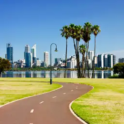 Vue de la skyline de Perth avec ses gratte-ciels depuis une promenade aménagée dans un parc bordé de palmiers.