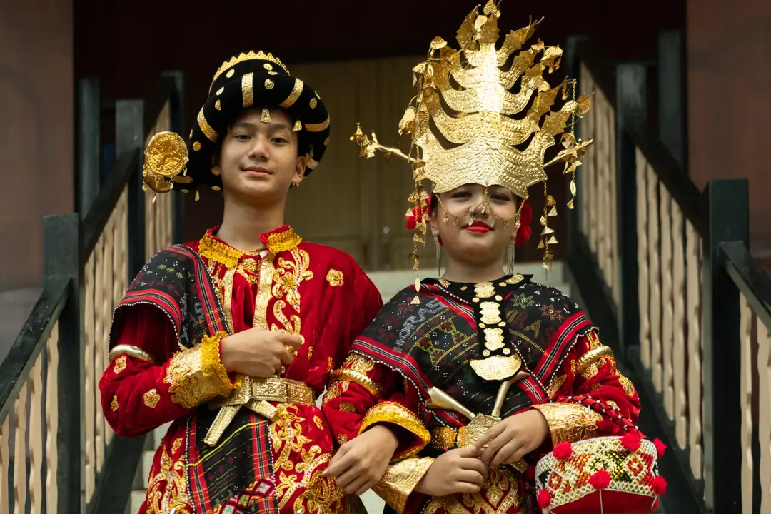 Voyage en Indonésie – Deux jeunes en costumes traditionnels Batak Toba ornés de broderies dorées, de tissus ulos et de coiffes d'apparat festives à Samosir.