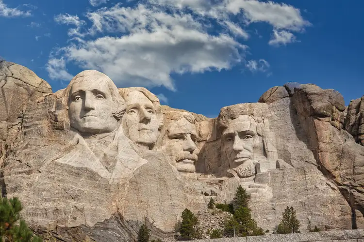Visages des présidents américains sculptés dans la falaise de granit du mémorial national du Mont Rushmore sous un ciel bleu parsemé de nuages