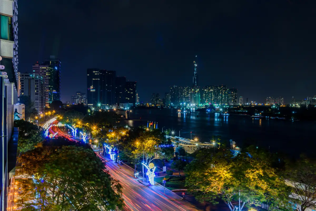 Voyage au Vietnam — Vue nocturne d’Hô Chi Minh avec gratte-ciel illuminés, circulation animée et Landmark 81 visible sur la rivière Saigon.