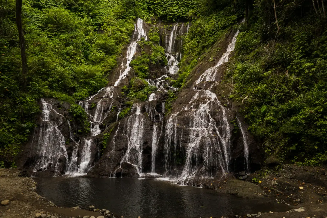 Voyage en Asie – Cascade aux multiples chutes d'eau s'écoulant le long d'une paroi rocheuse sombre entourée d'une végétation tropicale luxuriante à Bali en Indonésie.