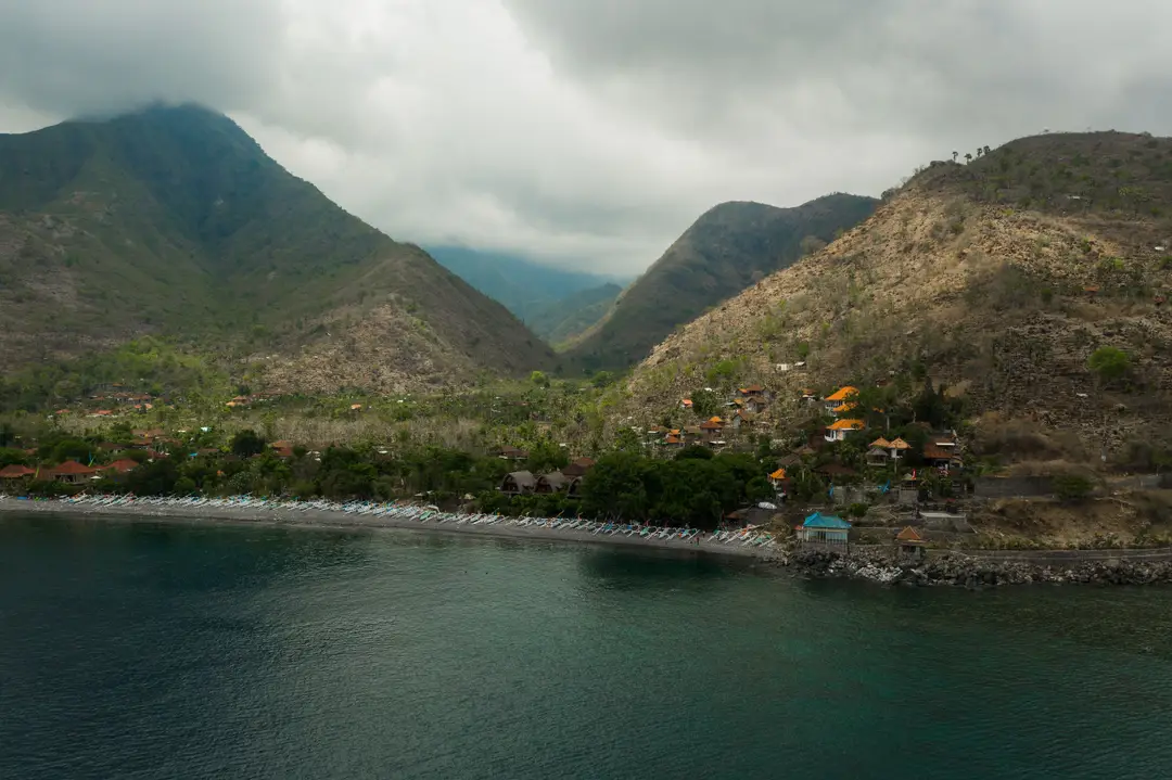 Bali hors des sentiers battus – Baie d'Amed vue du ciel avec ses pirogues jukung alignées sur la plage au pied des montagnes.