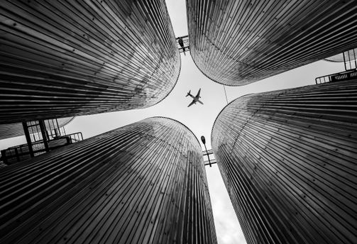 Travel in Asia - Low-angle perspective looking up at four large pillars, arranged to frame a single airplane flying overhead