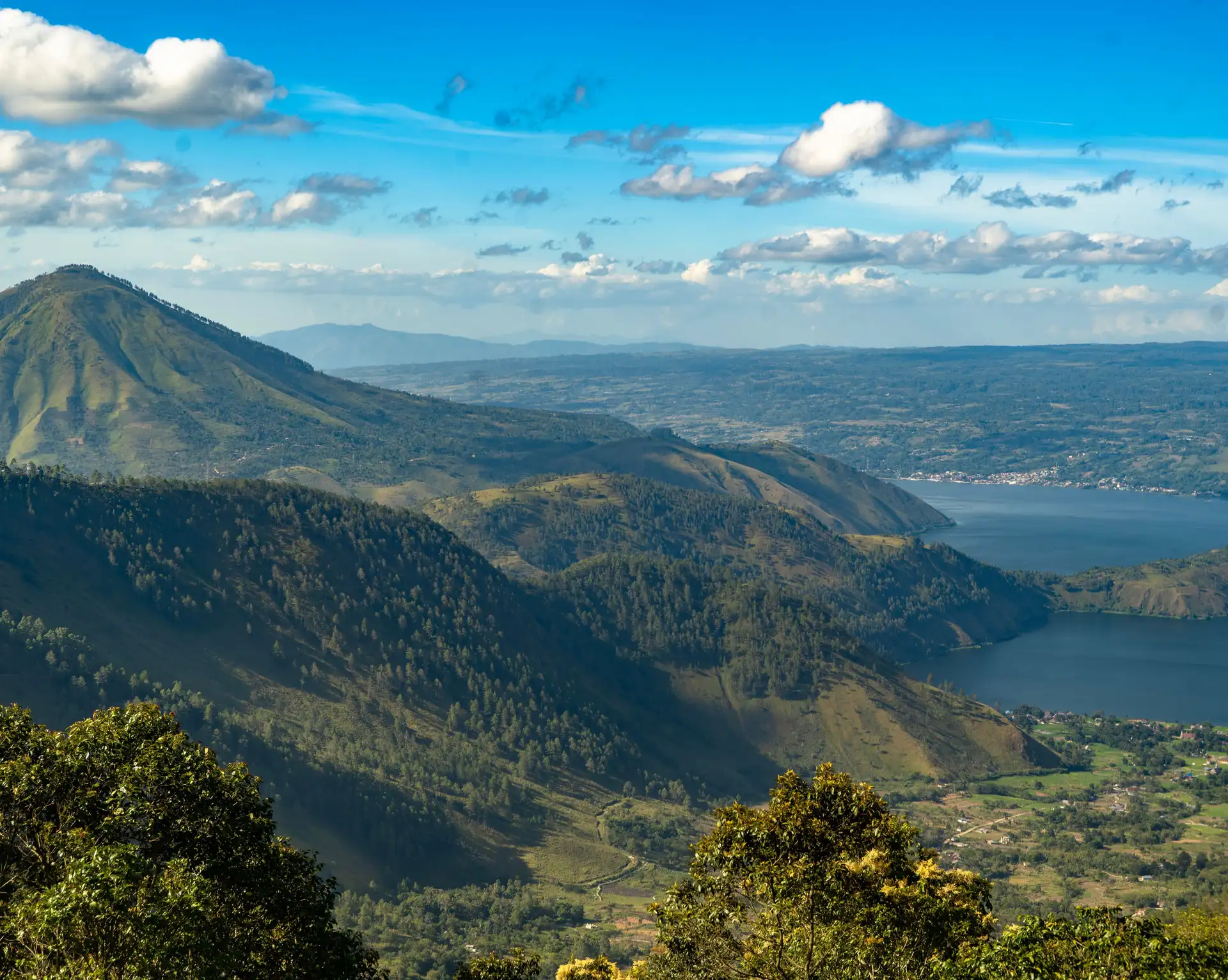 Voyage en Indonésie – Vue panoramique sur le lac volcanique Toba entouré de montagnes et de forêts tropicales sous un ciel bleu à Sumatra.
