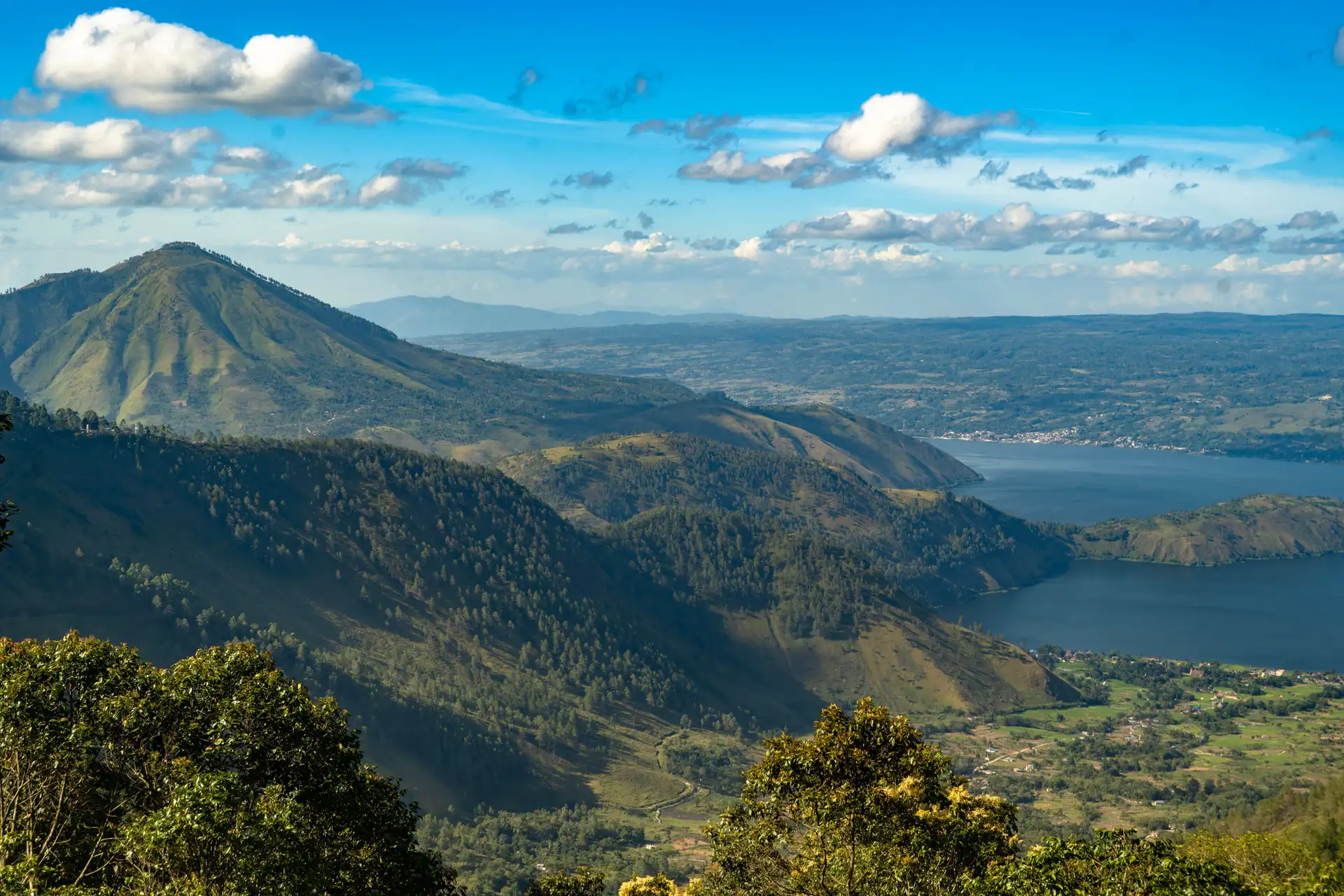 Voyage en Indonésie – Vue panoramique sur le lac volcanique Toba entouré de montagnes et de forêts tropicales sous un ciel bleu à Sumatra.