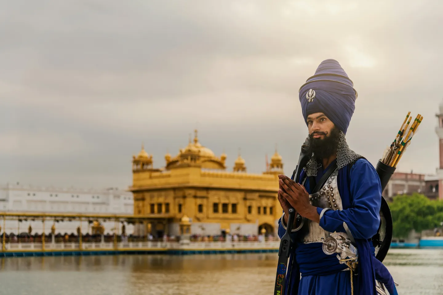 Portrait d'un guerrier Nihang Sikh en tenue traditionnelle bleue et armure devant le Temple d'Or (Harmandir Sahib) à Amritsar sous un ciel de fin de journée.