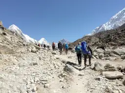 Groupe de randonneurs équipés de sacs à dos marchand sur un sentier rocailleux d'altitude face aux sommets enneigés de l'Himalaya au Népal.