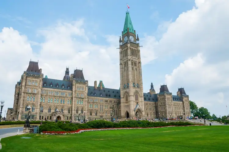 Édifice du Centre du Parlement canadien en pierre néogothique et sa Tour de la Paix bordés de pelouses à Ottawa