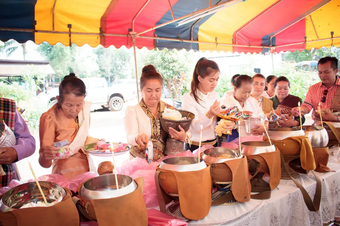 Fidèles laotiens déposant de la nourriture et des offrandes dans des bols à aumône alignés sous un chapiteau.