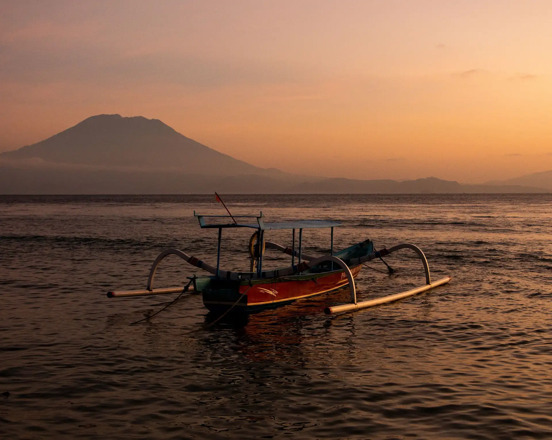 Voyage en Asie – Silhouette d'un bateau traditionnel balinais jukung voguant sur la mer calme face au mont Agung à l'aube à Bali.