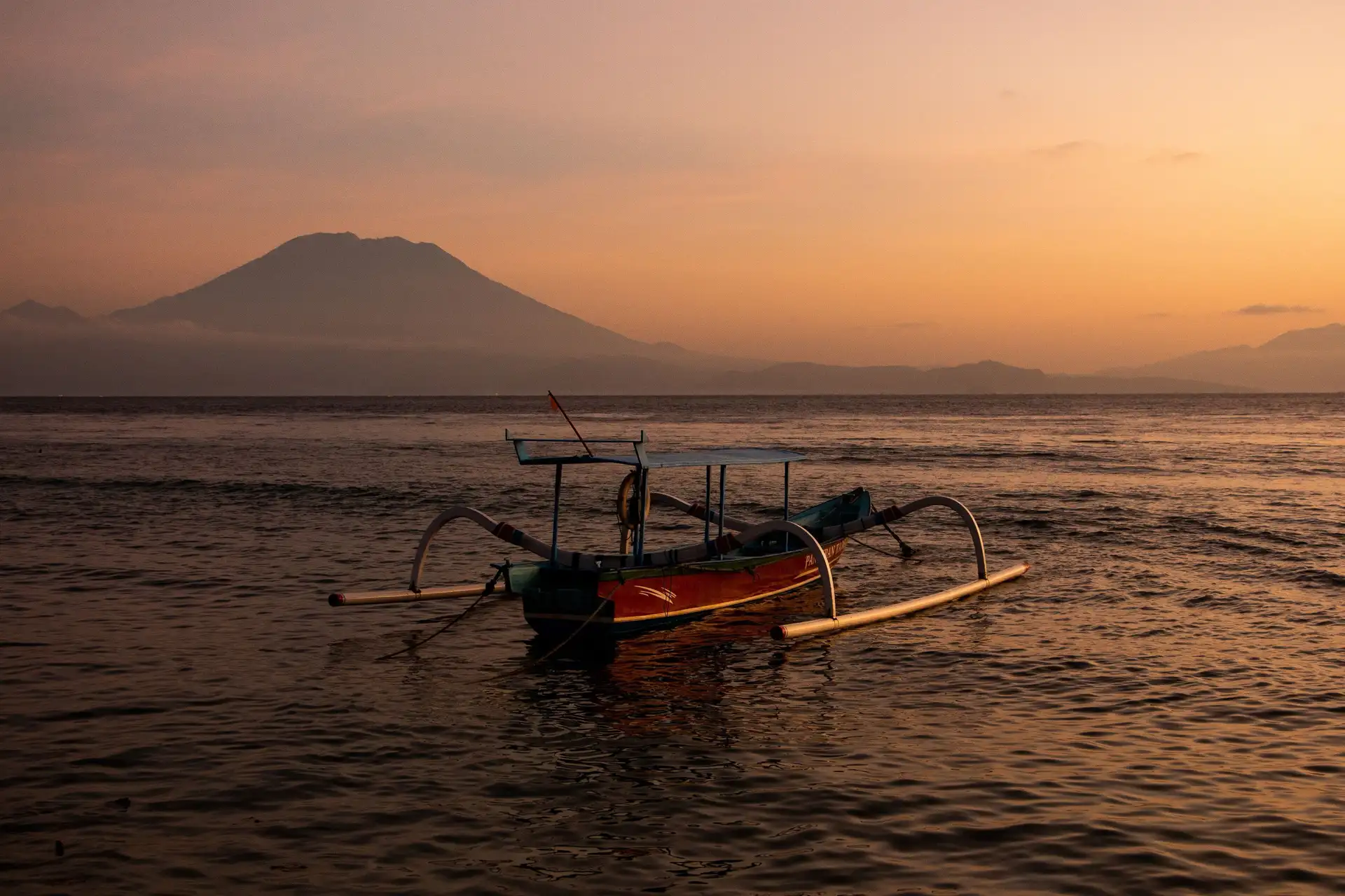 Voyage en Asie – Silhouette d'un bateau traditionnel balinais jukung voguant sur la mer calme face au mont Agung à l'aube à Bali.
