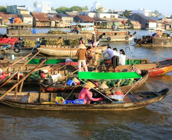 Voyage au Vietnam — Marché flottant animé du Delta du Mékong avec bateaux en bois, commerçants portant des Nón Lá et fruits locaux sur la rivière.