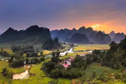 Jonque traditionnelle naviguant entre les pitons karstiques de la baie d'Along sous un ciel dégagé au Vietnam.