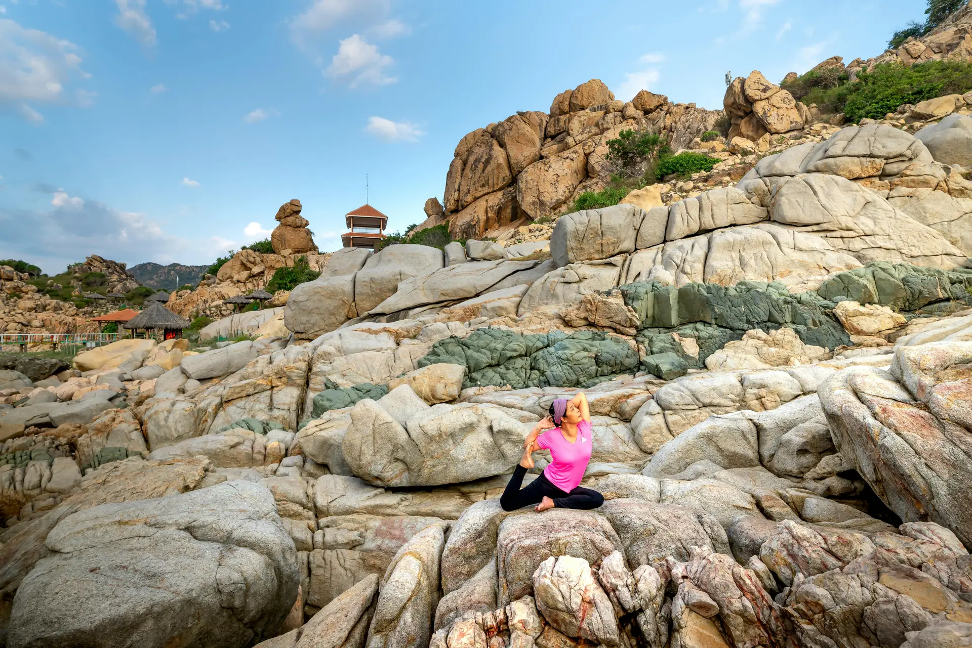 Une femme pratiquant le yoga en plein air sur des rochers côtiers sauvages au Vietnam sous un ciel clair.